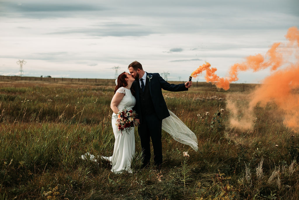 smoke bomb session - a groom holds a smoke bomb while he kisses his new bride in a open prairie field in southern Alberta.