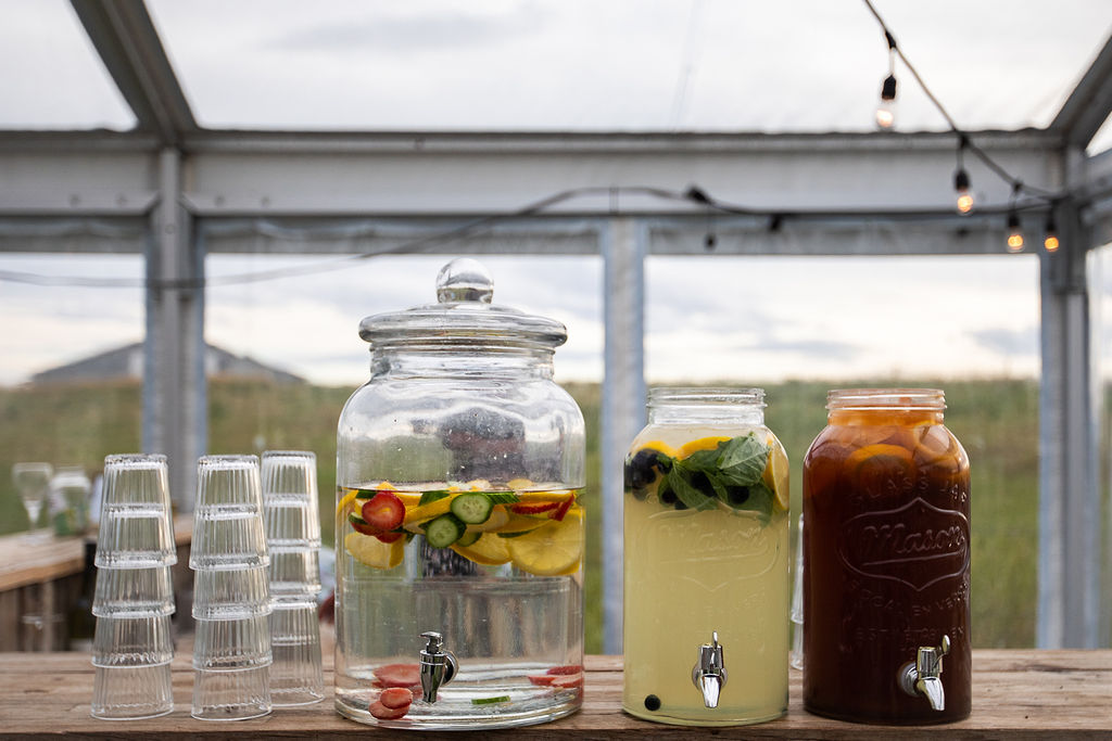 three juice dispensers filled with citrus, fresh herbs and veggies add a lovely touch to this outdoor wedding.