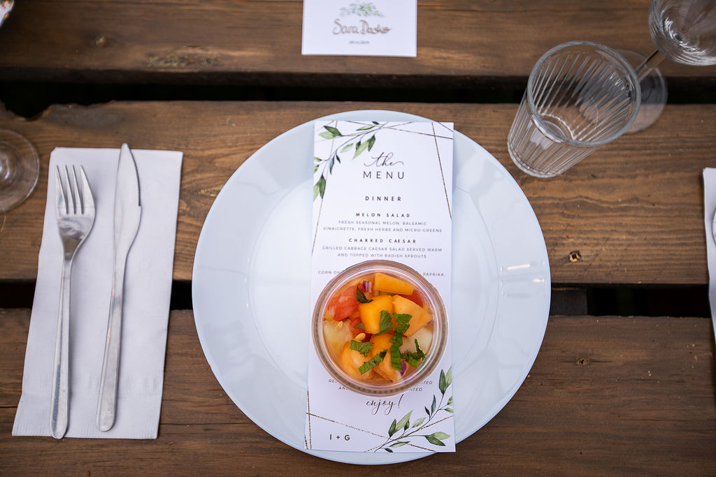 melon salad in a jar sits on a white plate with a menu card placed underneath.