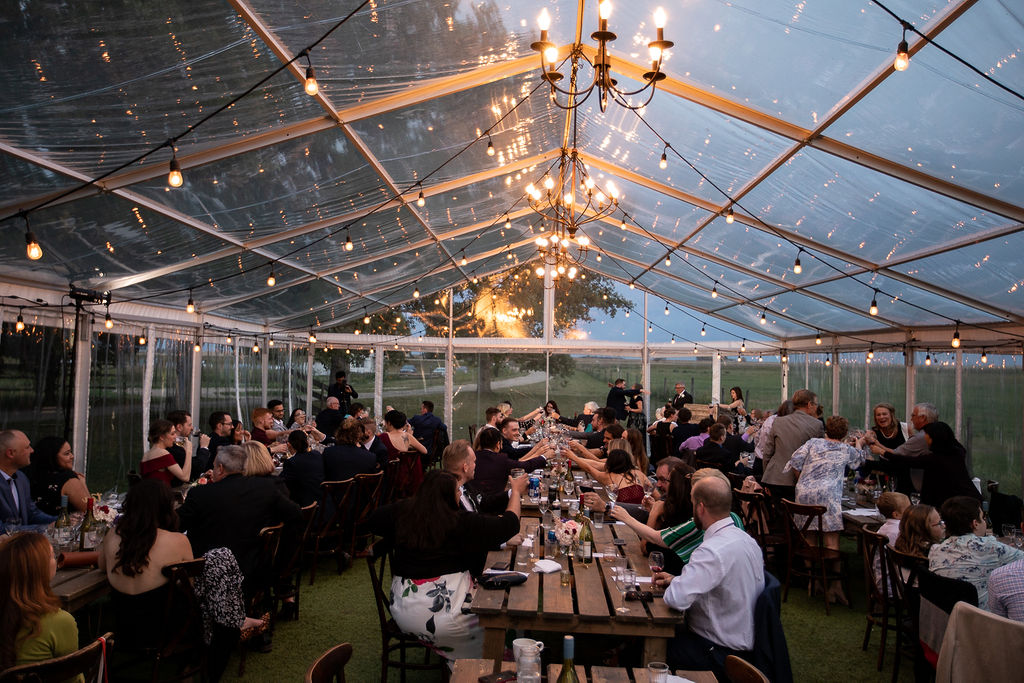 warm glowing lights highlight the clear tent at this outdoor wedding venue while guests mingle. www.thegathered.ca