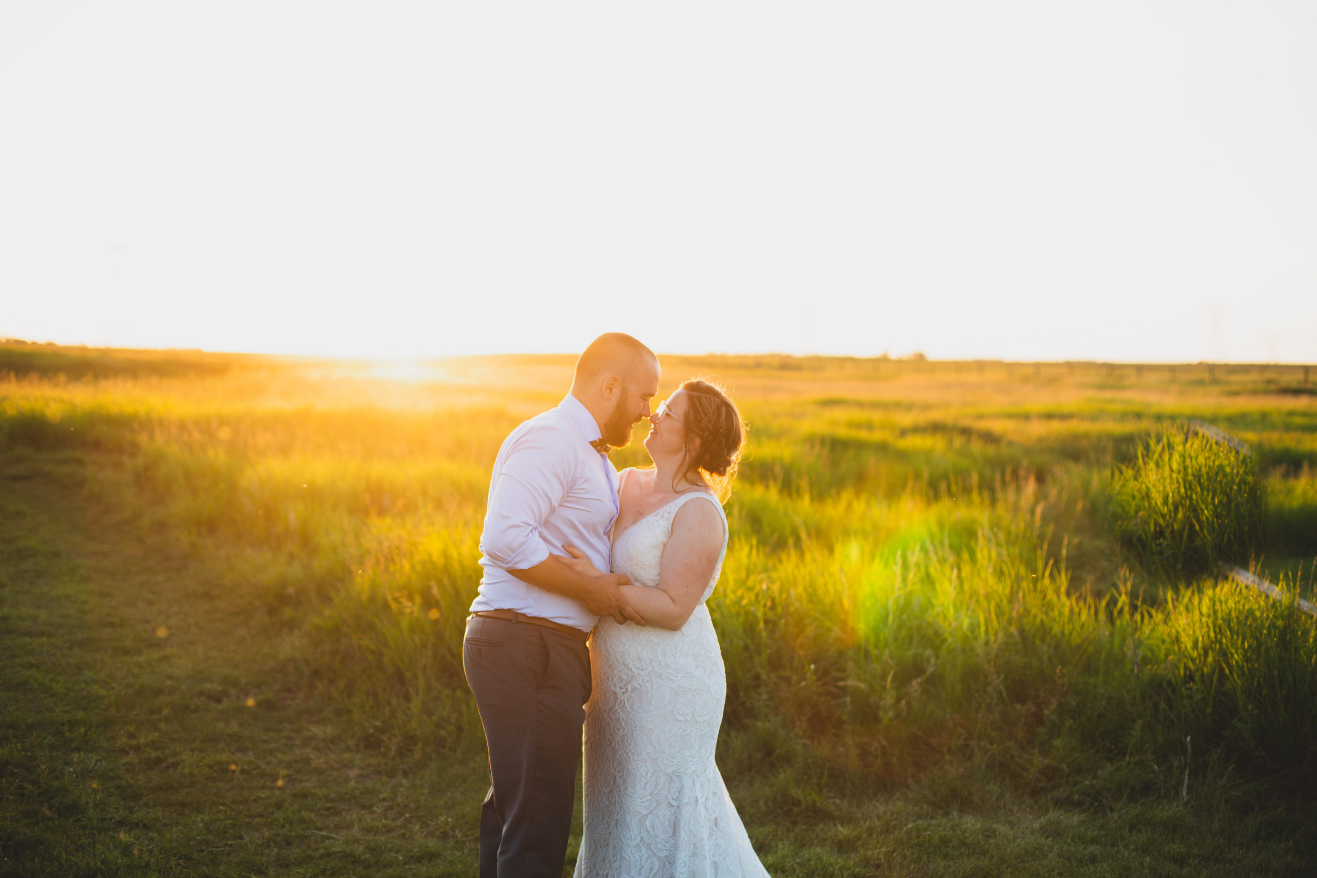A bride and groom sharing a tender kiss in a field bathed in golden hues at sunset.