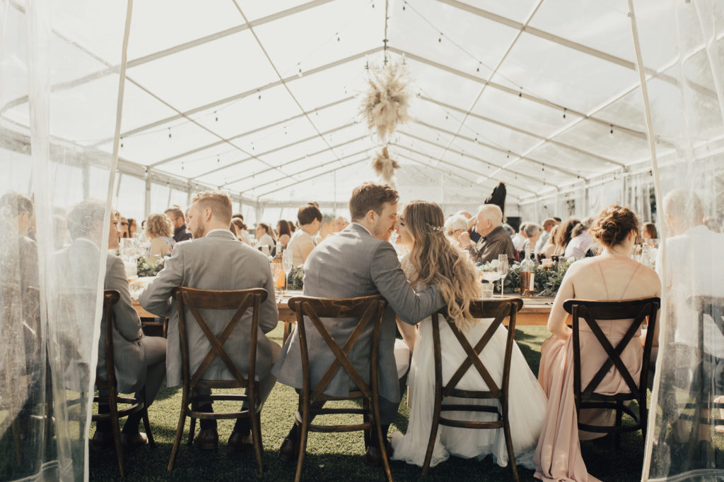 modern wedding with a flair, couple kisses during their wedding reception under a clear tent with pampas hanging pieces