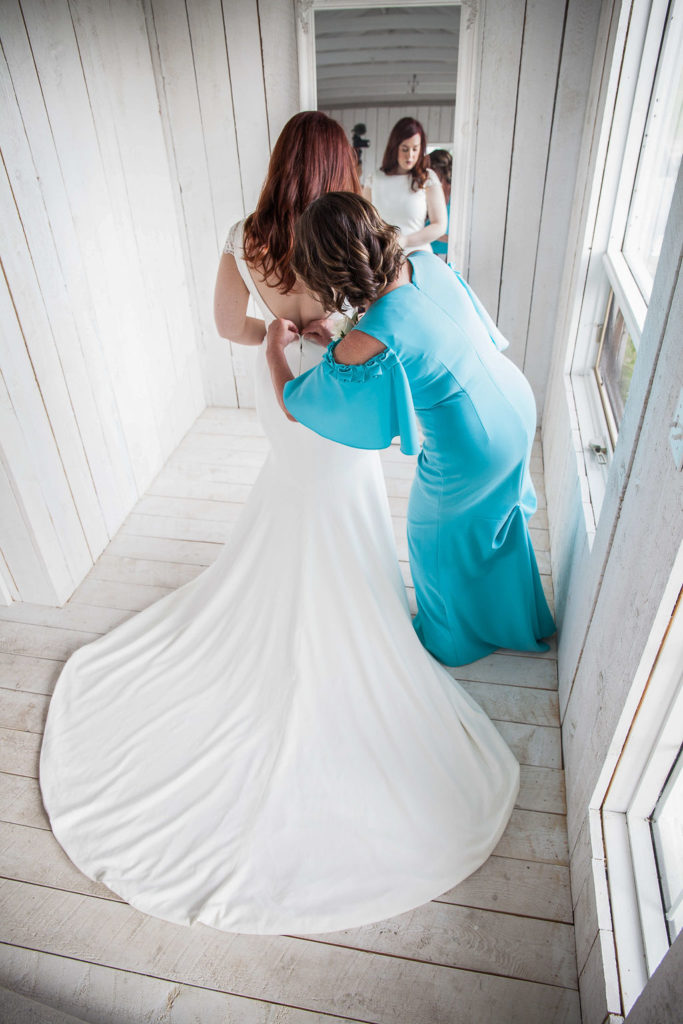 mother of the bride buttons up the brides dress in an white cottage