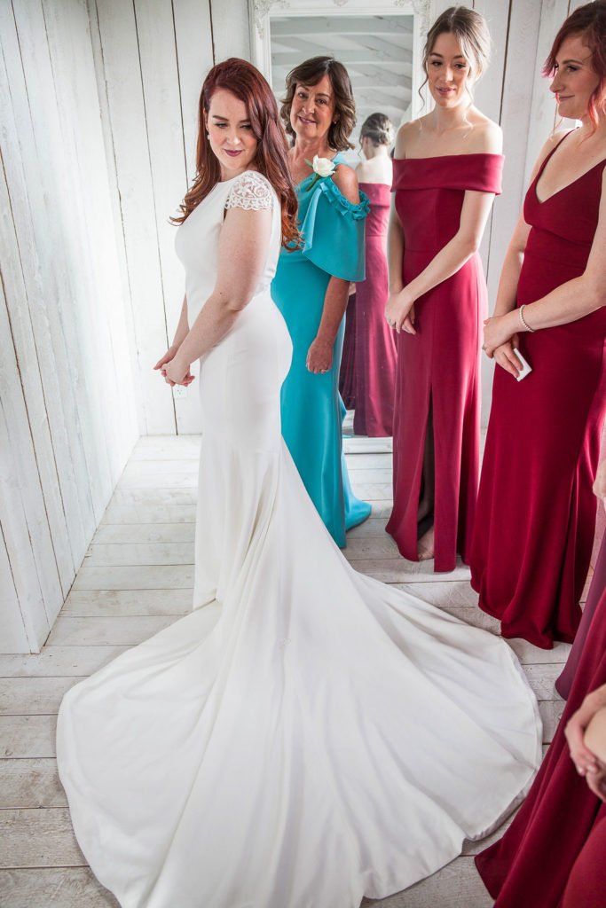 bride shows off her dress and bridesmaids in burgundy dresses surround her.