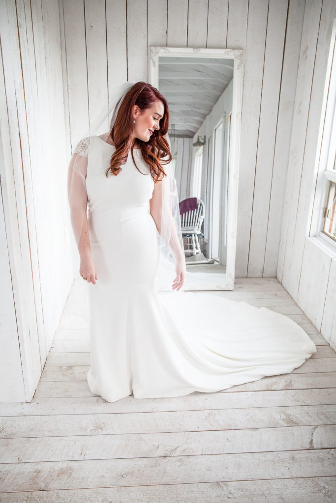 bride in a classic wedding dress with capped sleeves stands in a white panelled cottage. thegathered.ca