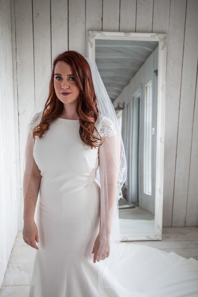 bride in a classic wedding dress with capped sleeves stands in a white panelled cottage. thegathered.ca