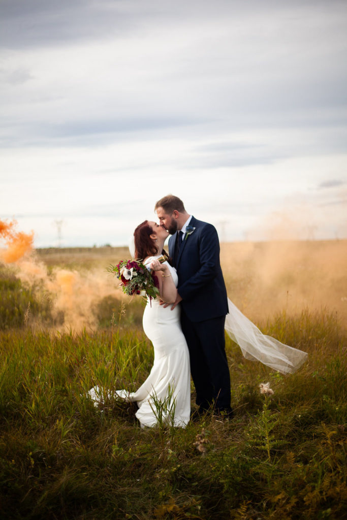 smoke bomb session - a groom holds a smoke bomb while he kisses his new bride in a open prairie field in southern Alberta.
