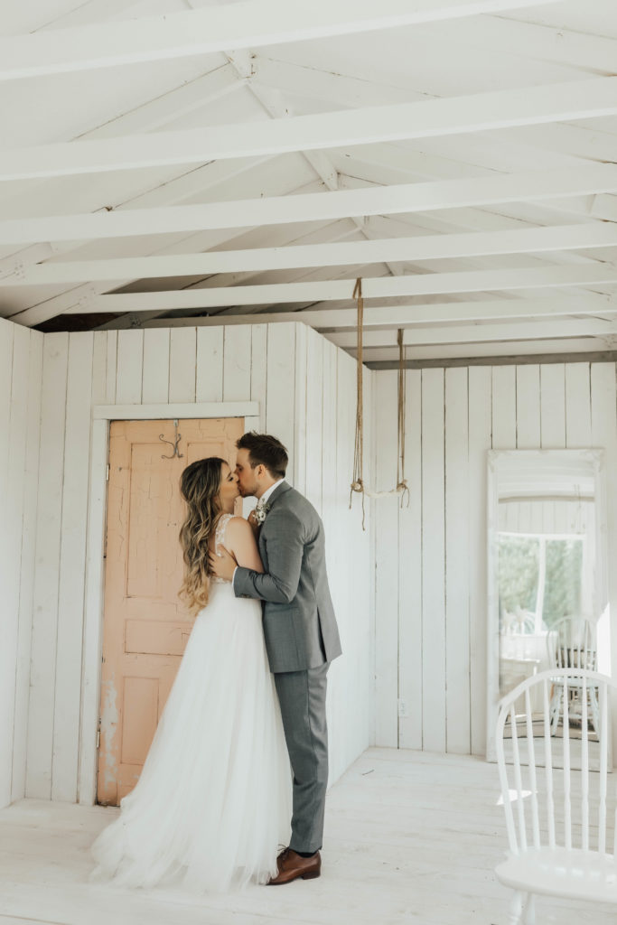 modern wedding couple kiss inside a white cottage with a blush pink door. www.thegathered.ca