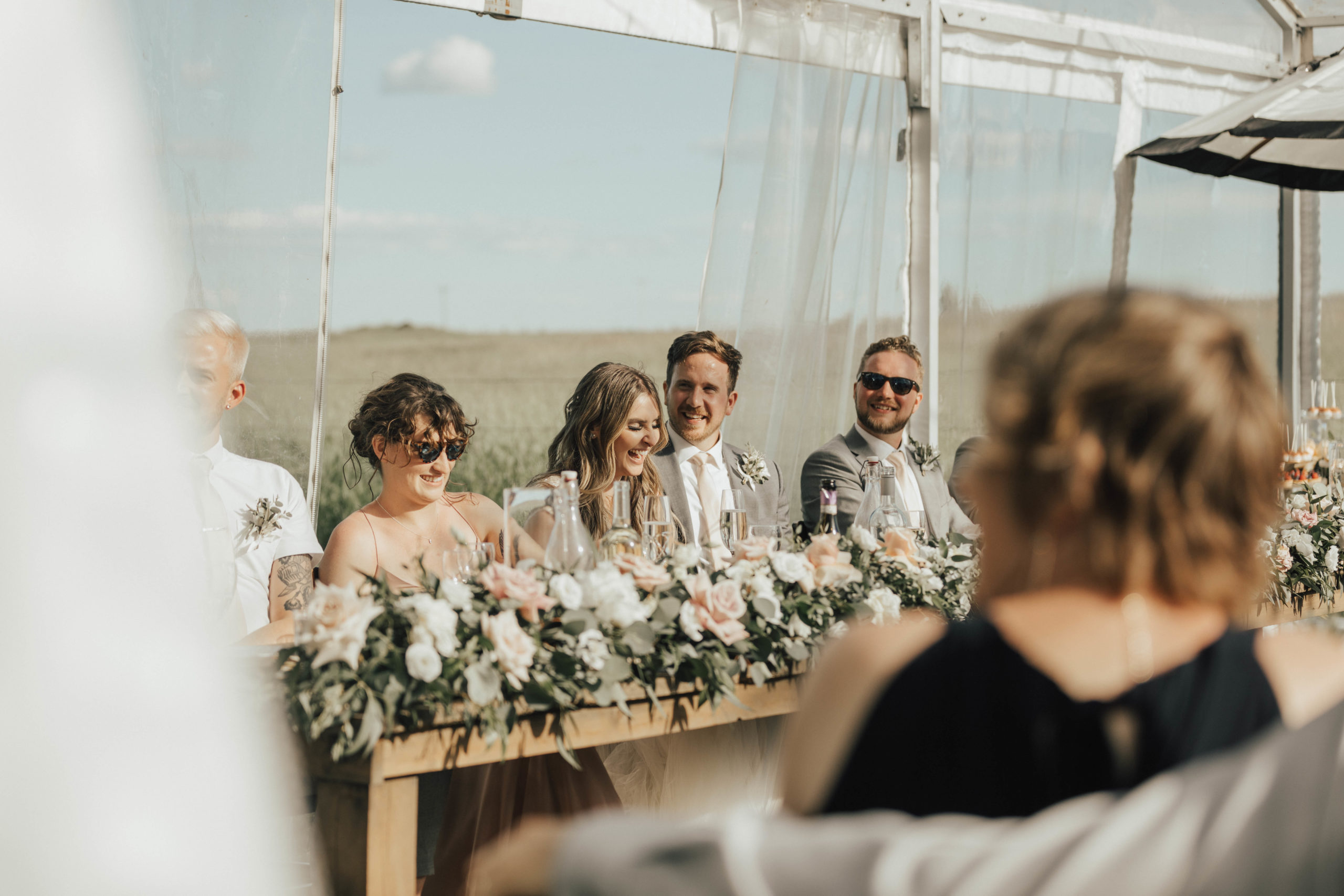 bridal party laugh during speeches at this outdoor tented wedding in the prairies.