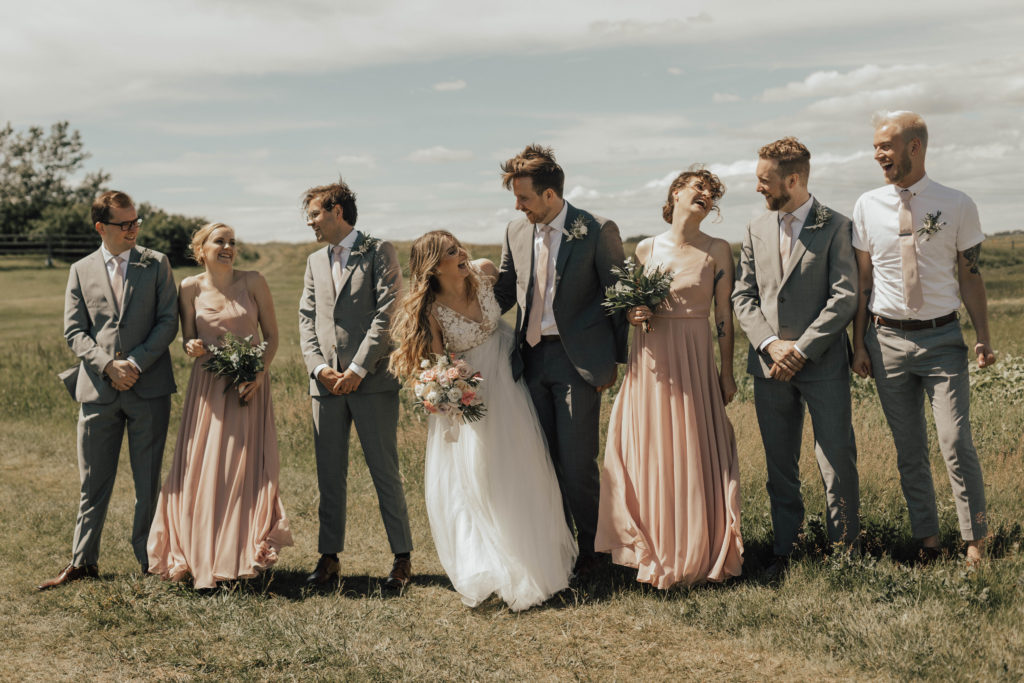 bridal party walk through a field with the girls in blush pink and the guys in grey suits.