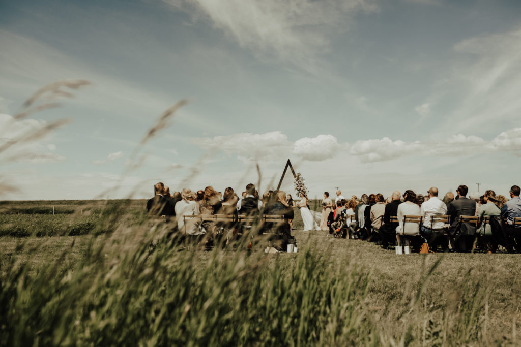 guests seated at an outdoor wedding ceremony in a prairie field with bright skies and modern flair decor. www.thegathered.ca