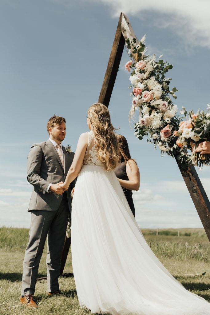 triangle arbor decorated with pink and white flowers make a perfect backdrop for this romantic wedding at an outdoor ceremony. www.thegathered.ca