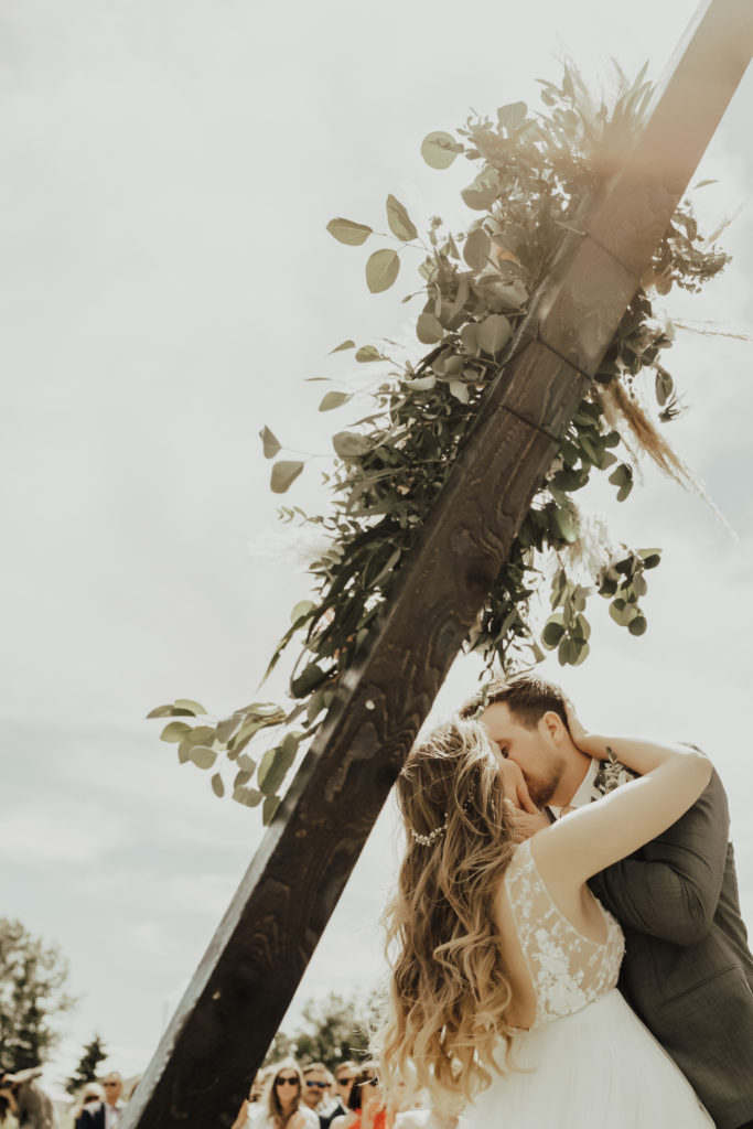 first kiss as husband and wife under a wood triangle arbor with greenery.
