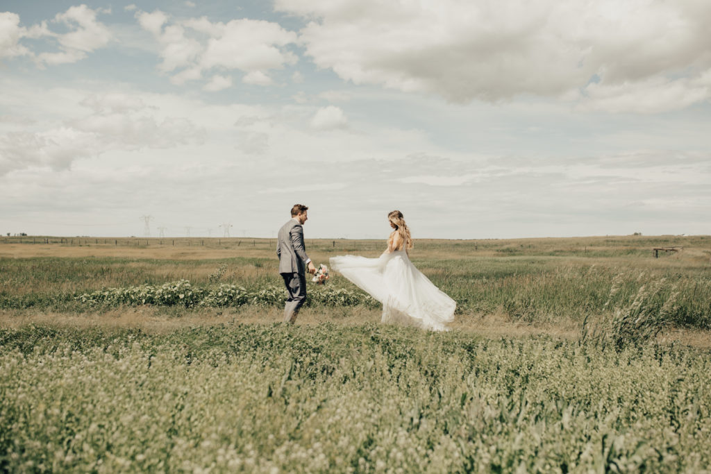 romantic modern wedding dress twirls in the wind as the bride and groom dance in a prairie field of their outdoor wedding. www.thegathered.ca
