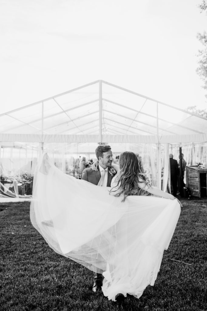bride twirls her dress with her arm around the groom as they stand outside their outdoor tented wedding reception. www.thegathered.ca