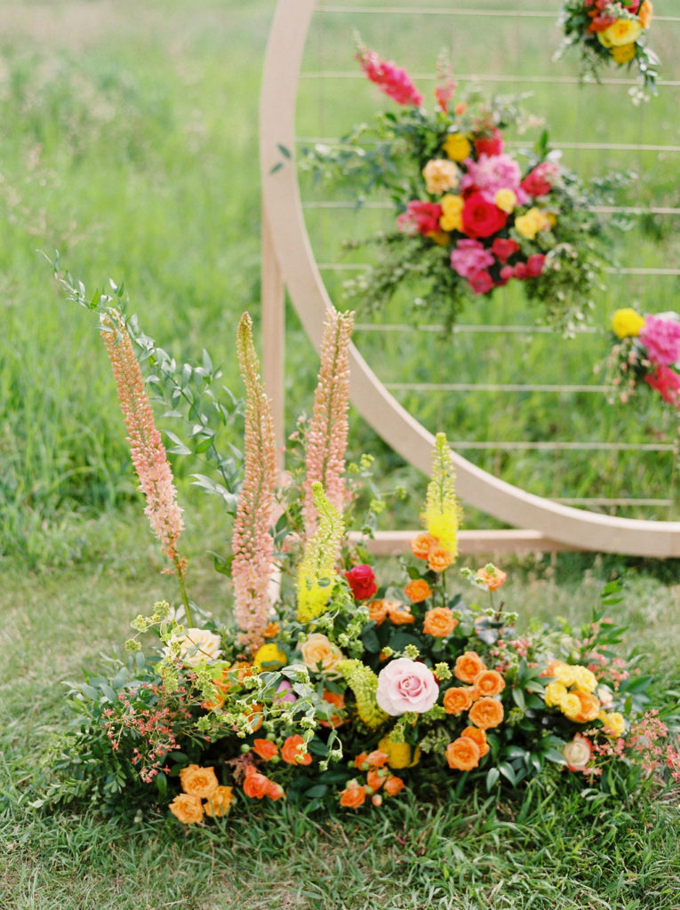bold orange pink and yellow flowers designs sit in a green field beside a circular arbor