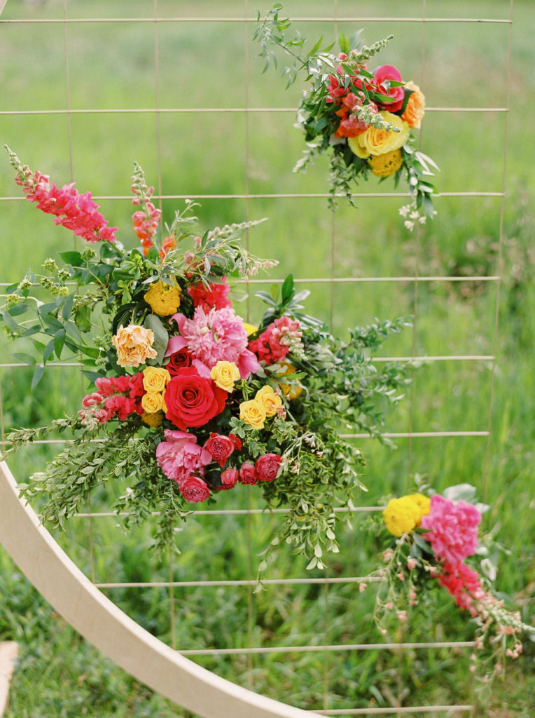 bright red, pink and yellow flowers decorate an arbor against a grassy backdrop