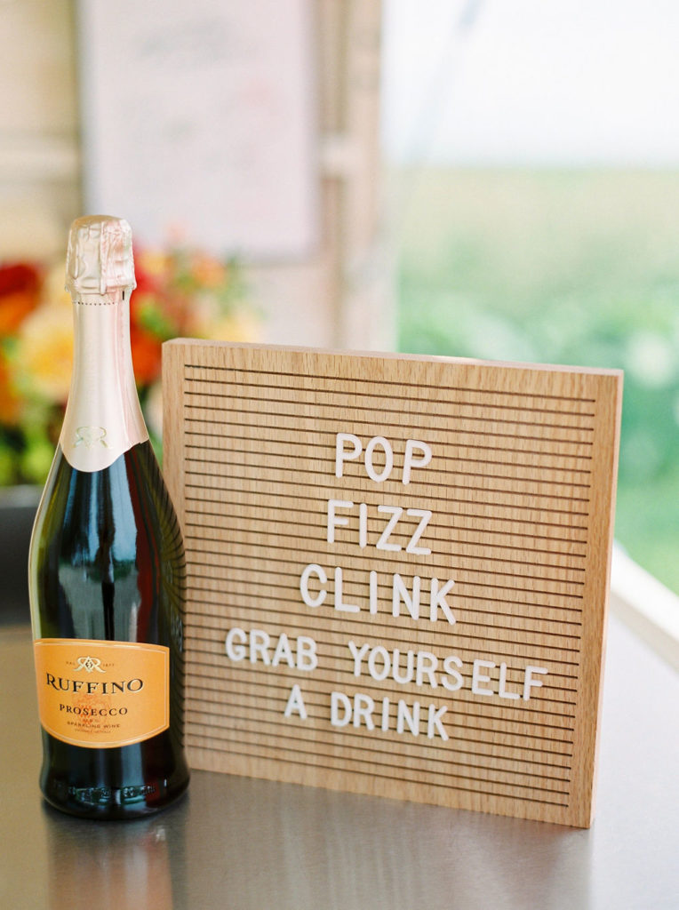 wood letter board that says pop fizz clink grab yourself a drink which sits beside a bottle of prosecco
