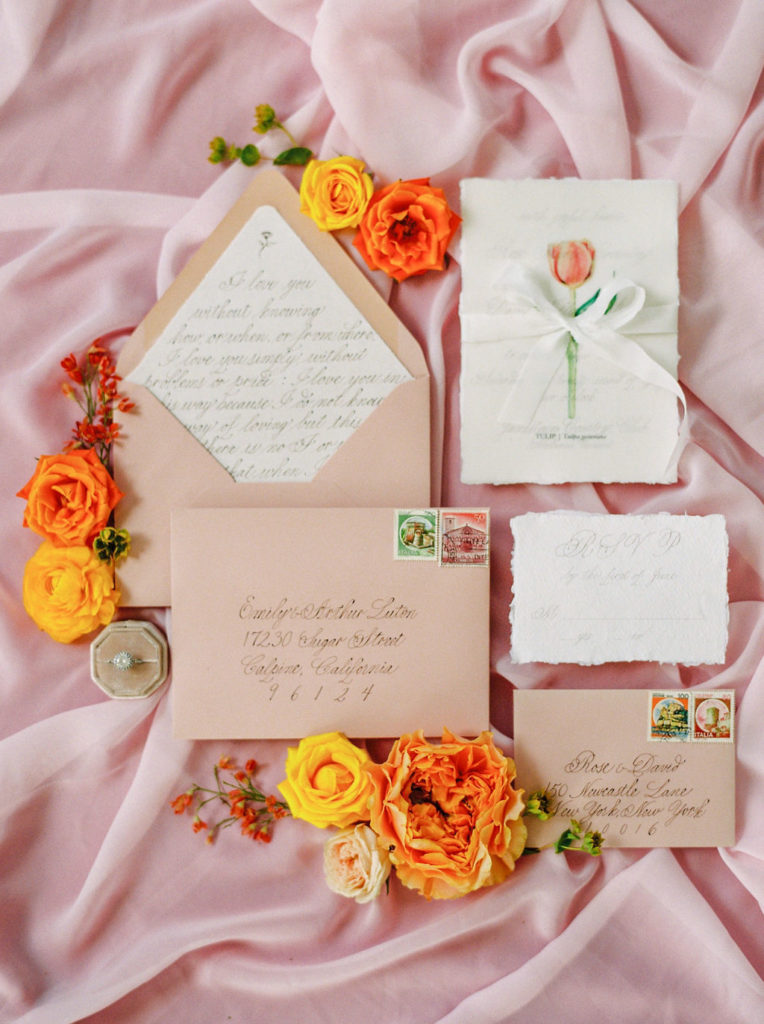 flat lay of pink and white invitations and orange and yellow flowers