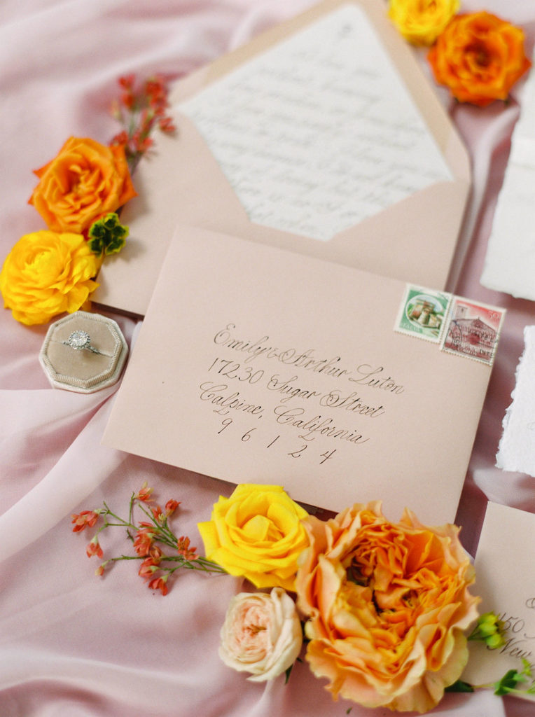 flat lay of pink and white invitations and orange and yellow flowers
