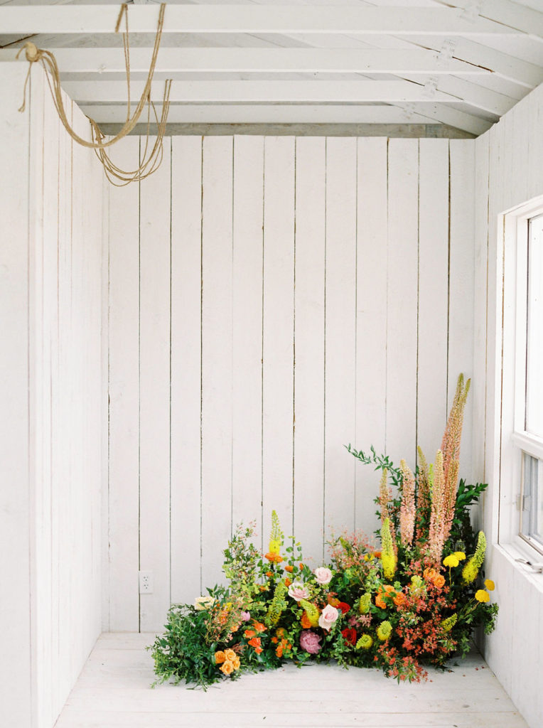 white cottage room with a large green, orange and pink floral arrangement lines the floor