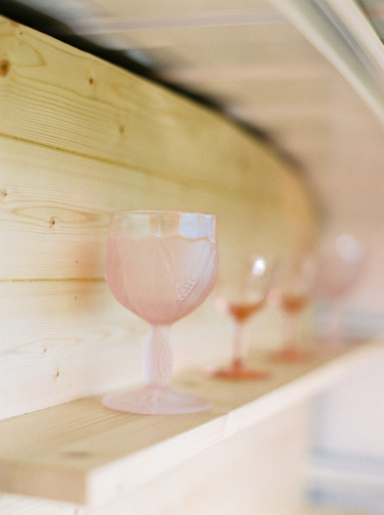 blush pink wine goblets stand on wood shelf