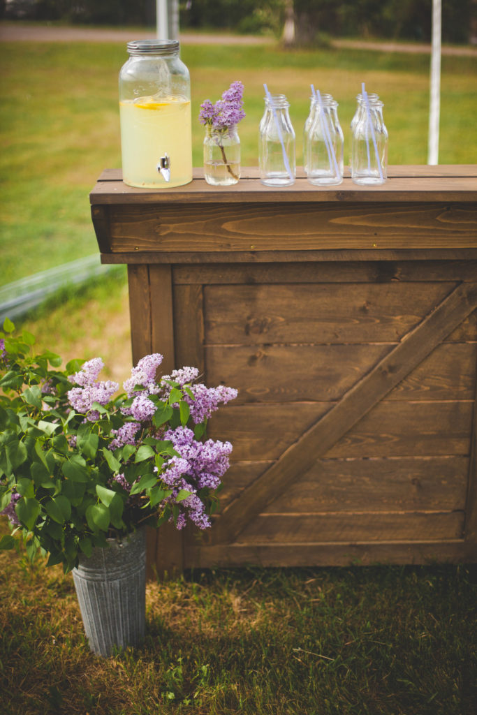 wooden outdoor bar with lilac lemonade and lilac flowers as decor thegathered.ca
