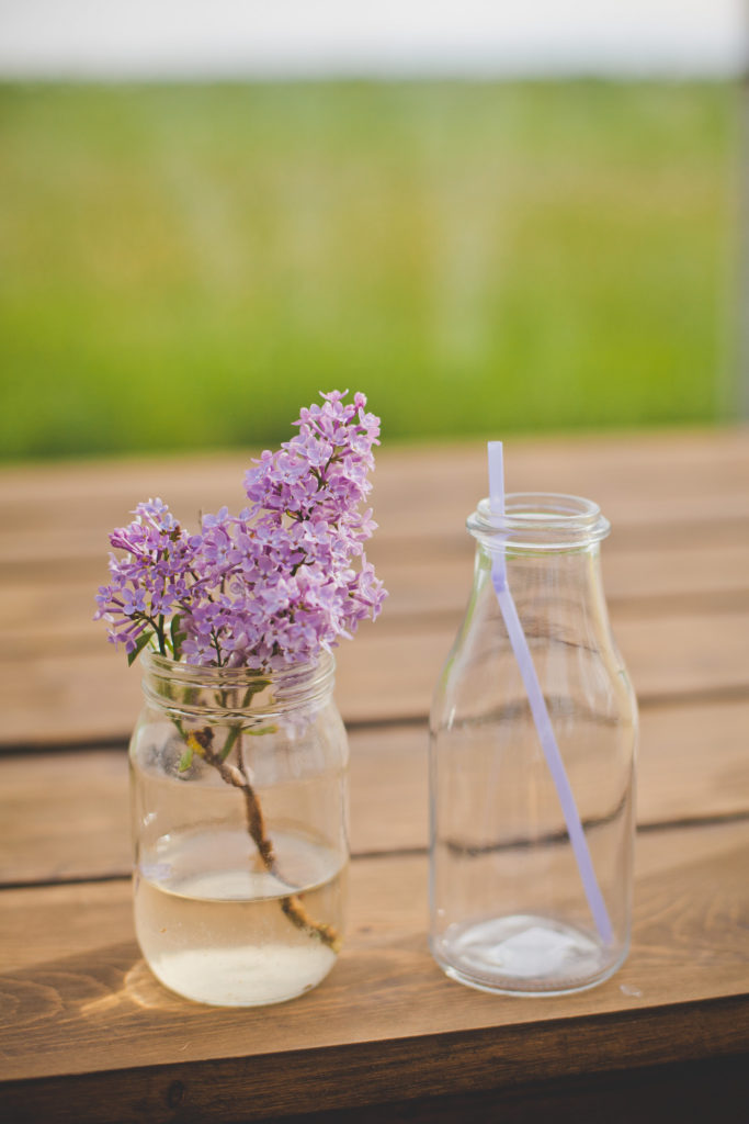 lilacs in a jar beside a drinking milk bottle jar