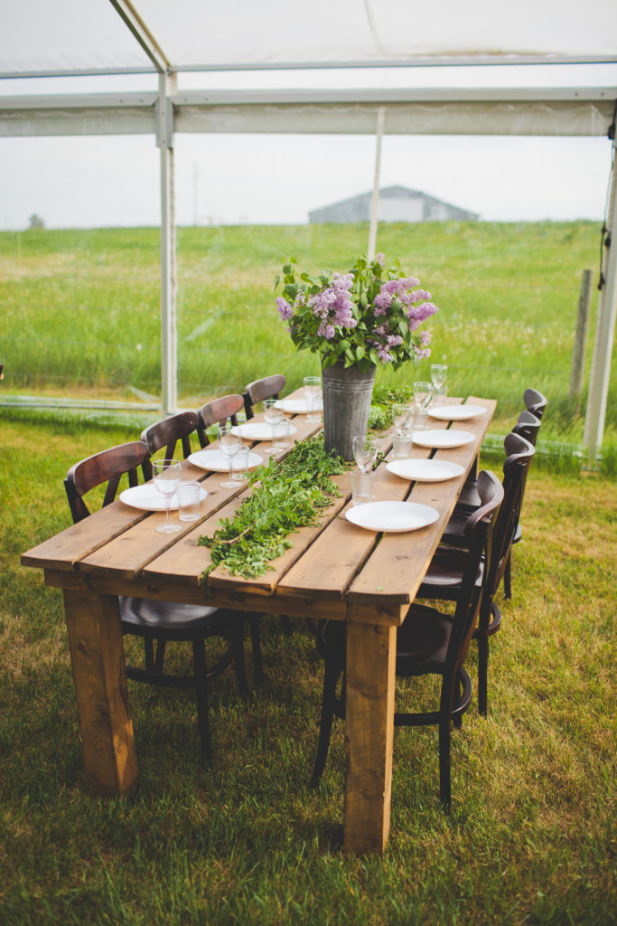 a wood harvest table with lilac flowers in a galvanized buckets and rows of greenery on the tables.