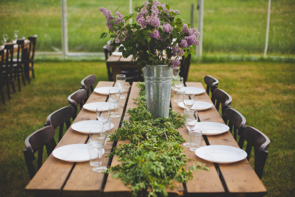 lilacs in galvanized buckets with rows of greenery decorate wood tables for this outdoor wedding.