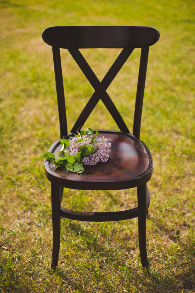 wood cross back chair on a grassy lawn with a single lilac placed on the chair