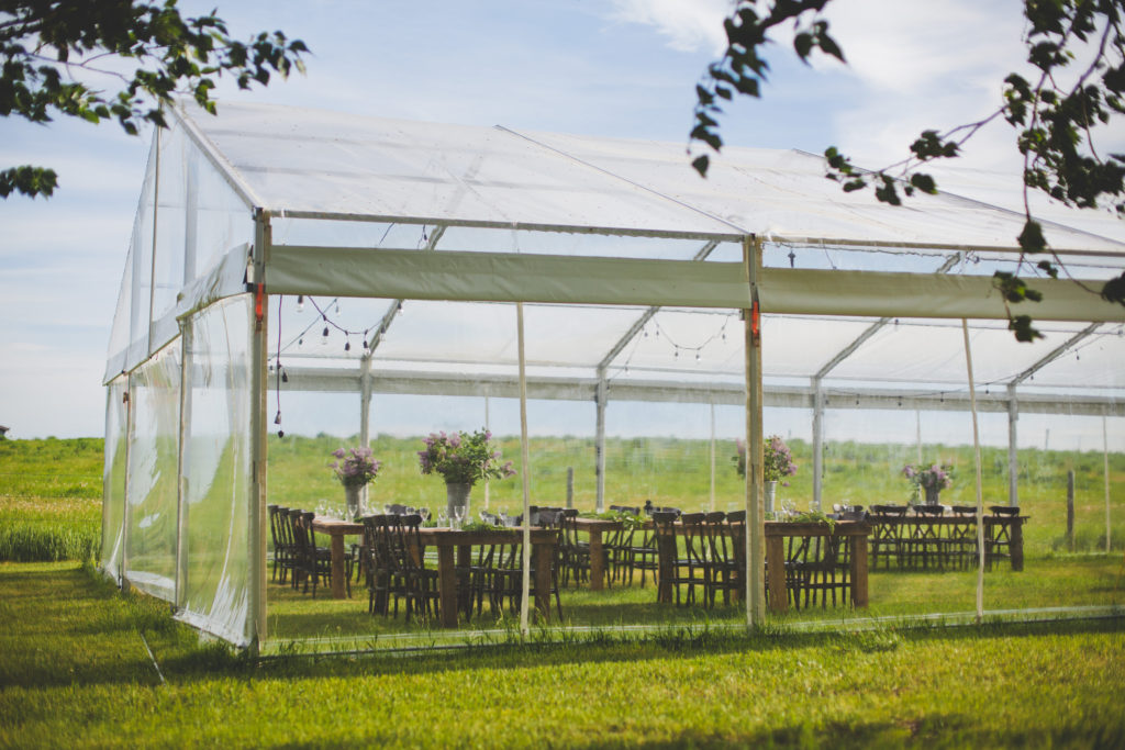 outdoor clear tent wedding - wood tables and chairs all placed in a open prairie field www.thegathered.ca