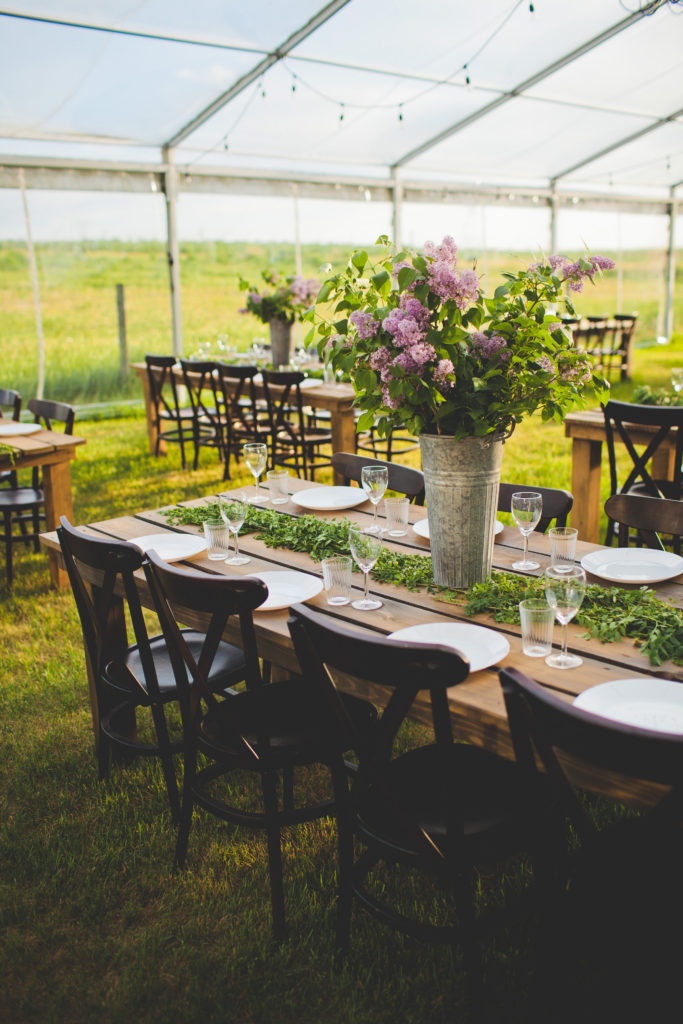 wood crossback tables and chairs at an outdoor wedding in the prairies with lilac flowers in galvanized buckets. www.thegathered.ca