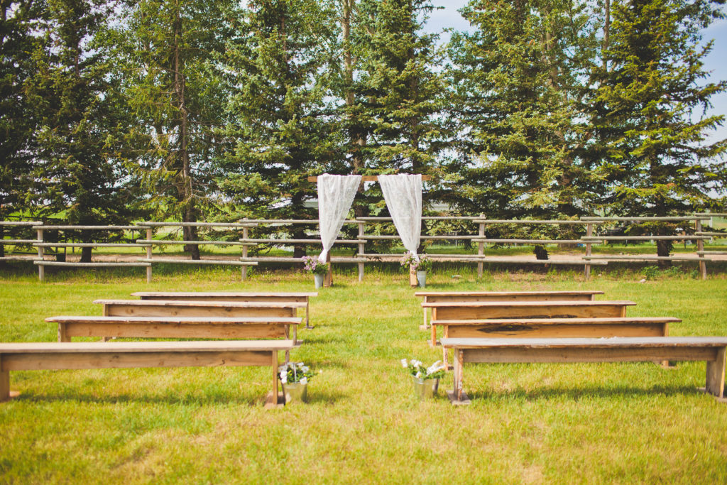 tree ceremony space with white lacy curtain arbor and wood benches