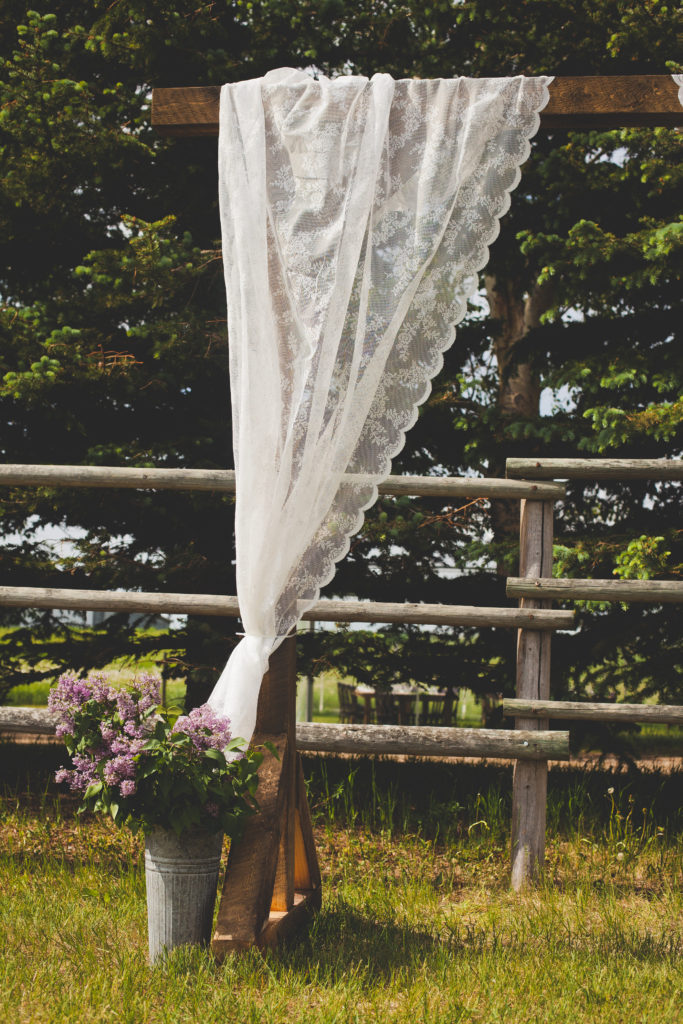 wood arbor decorated with white lace curtains and lilacs