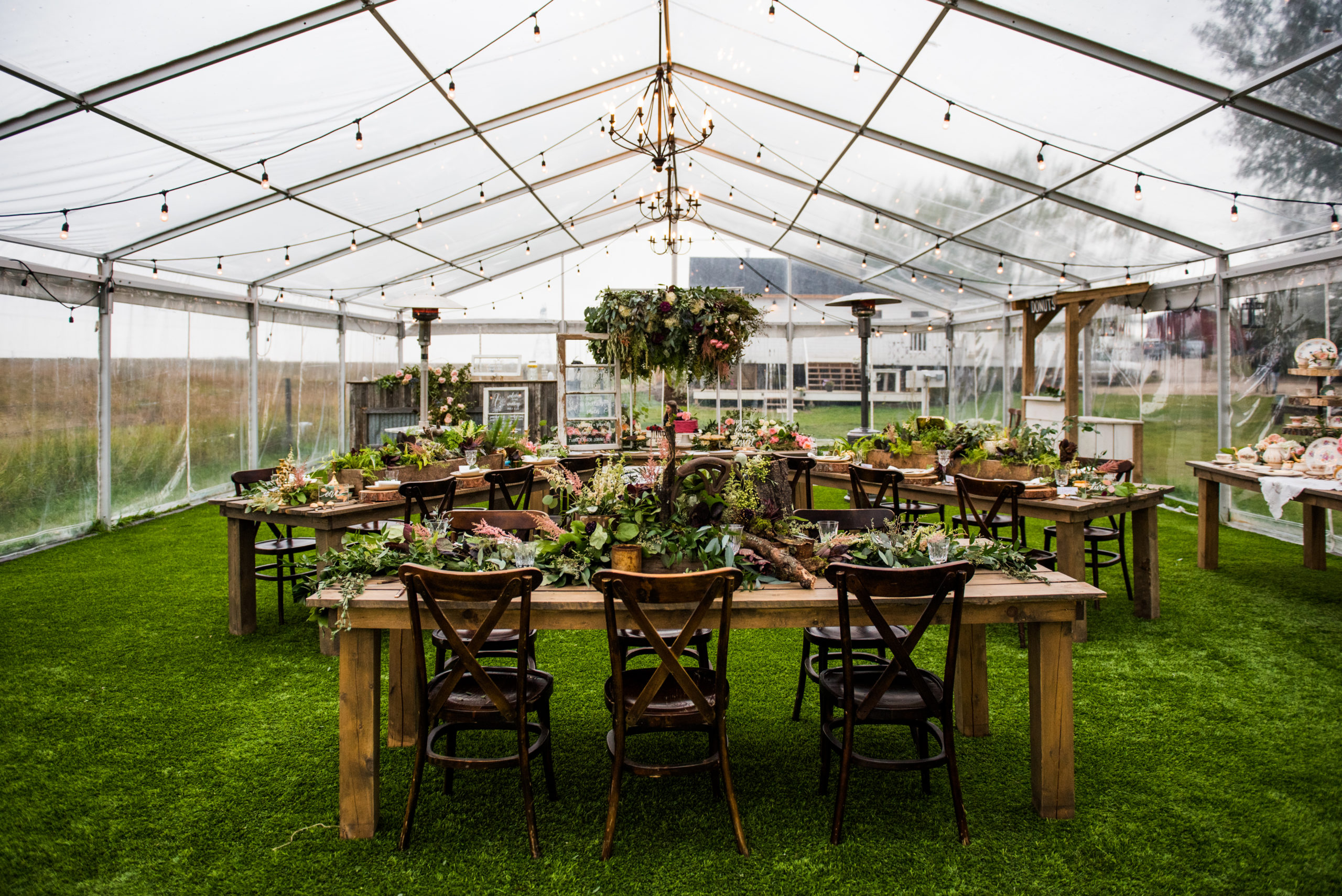 wedding reception set up for an intimate wedding with covid restrictions. Decorated with wild greens and earthy fixtures set in a clear tent with hanging globe lights.