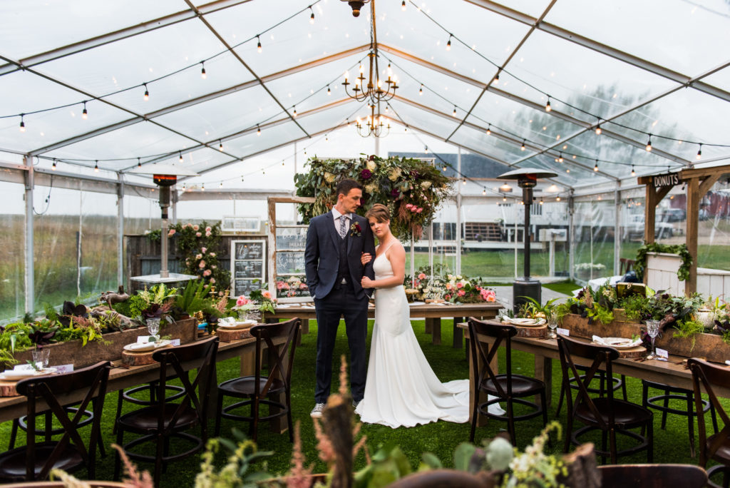 a unique way of setting up for a intimate wedding or elopement. The tables are set with wild flowers and greenery inside of a clear tent with hanging chandeliers