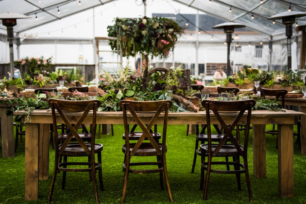 weddings decorated with objects from nature and greenery. Wood tables and crossback chairs in a outdoor tent