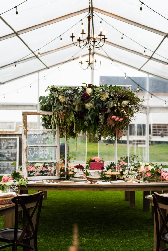hanging flowers over a dessert table in a clear tent with hanging chandeliers