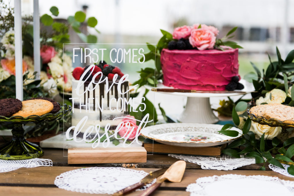 dessert sign "first comes love then comes dessert" sitting on a dessert table with a pink frosted cake and vintage china