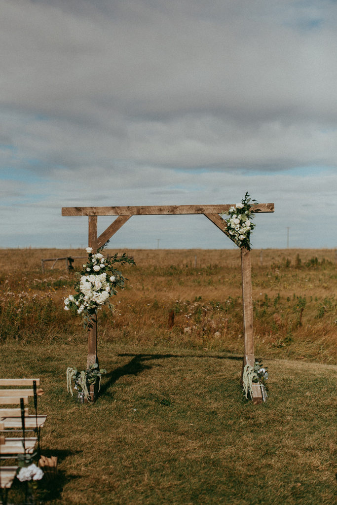 wedding arbor standing in a prairie field decorated with white and green flowers