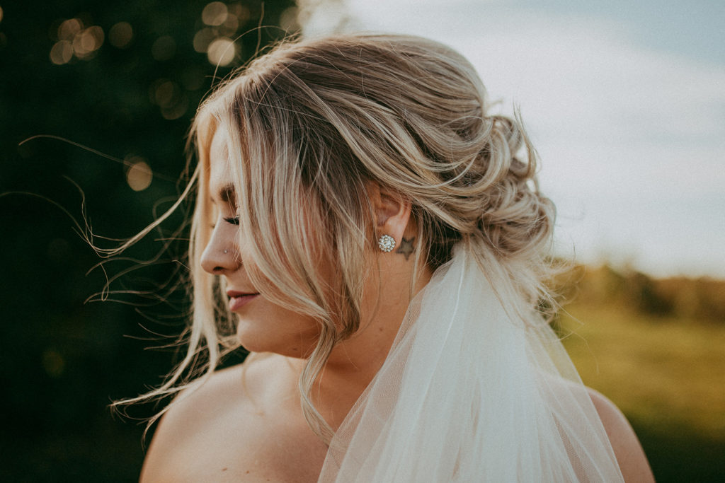 closeup of the bride looking off to the side showing her earrings and long field tucked beneath her blonde low cascading updo