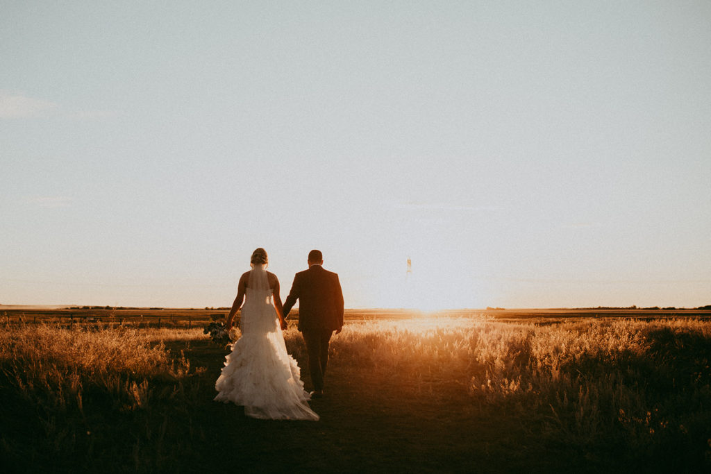 a wedding couple walk into a field and the sun sets and creates a gorgeous golden hour