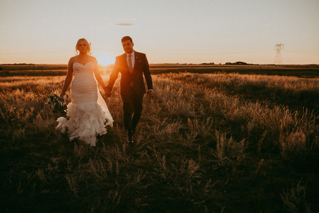 bride and groom walk hand in hand through a fall field path at this outdoor wedding venue in calgary alberta
