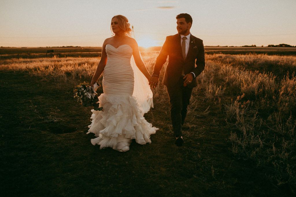 a warm golden fall inspired prairie field makes the perfect backdrop as the bride and groom walk holding hands