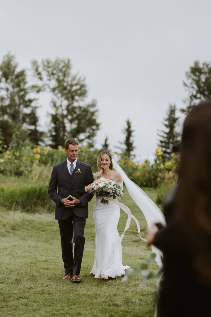 bride and father walking down a grassy floral path