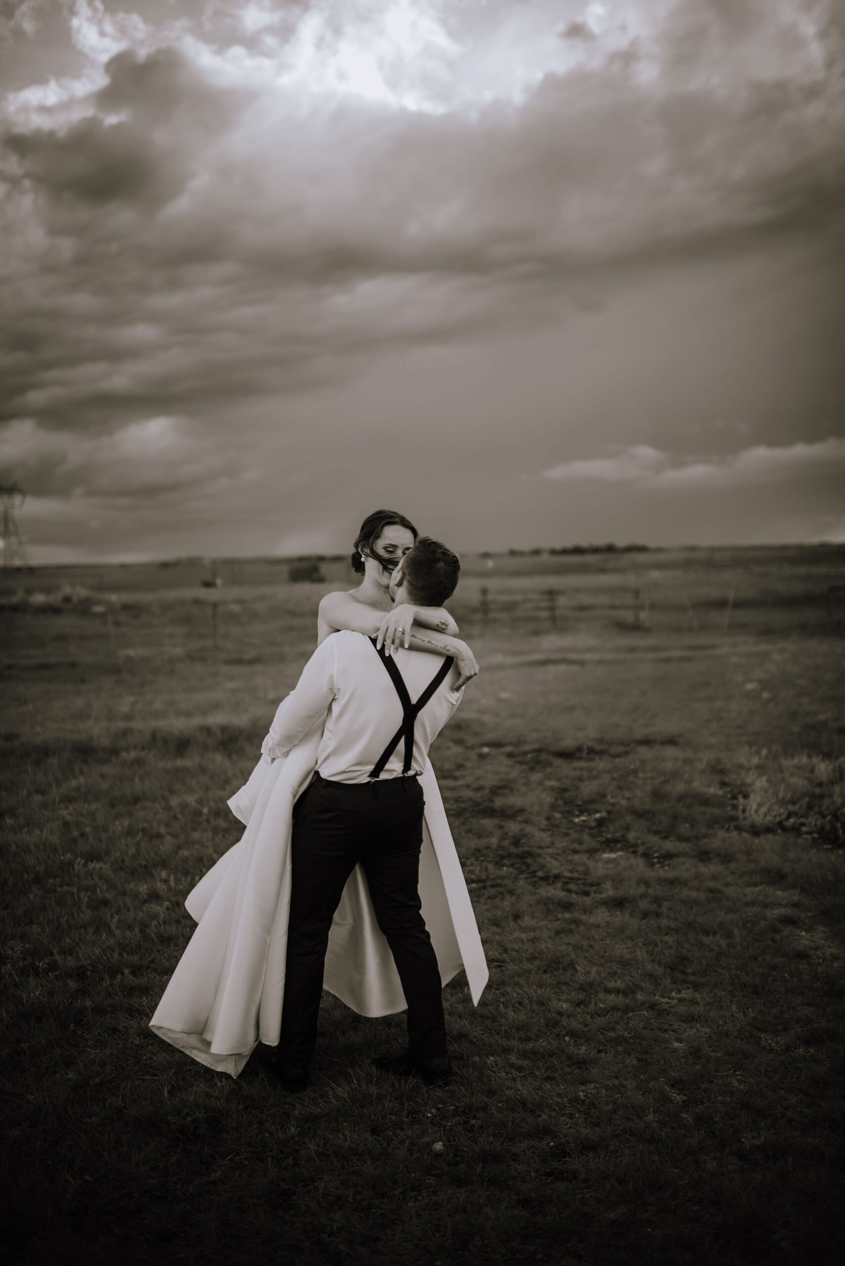 A bride and groom passionately hugging in a field under a stormy sky, symbolizing their eternal June love.