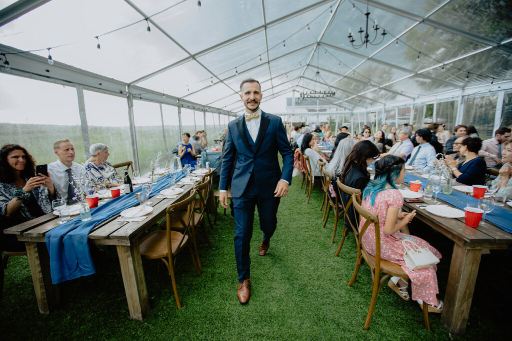 A man walking down the aisle at a wedding reception in a tent.