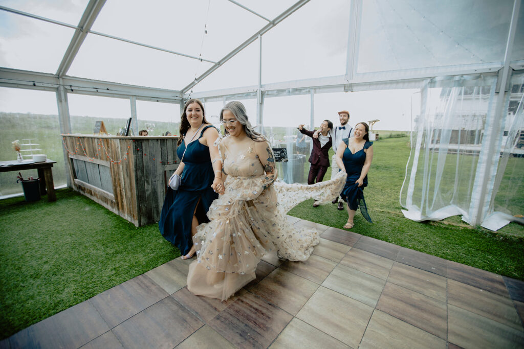 A bride and her bridesmaids walk through a tent.