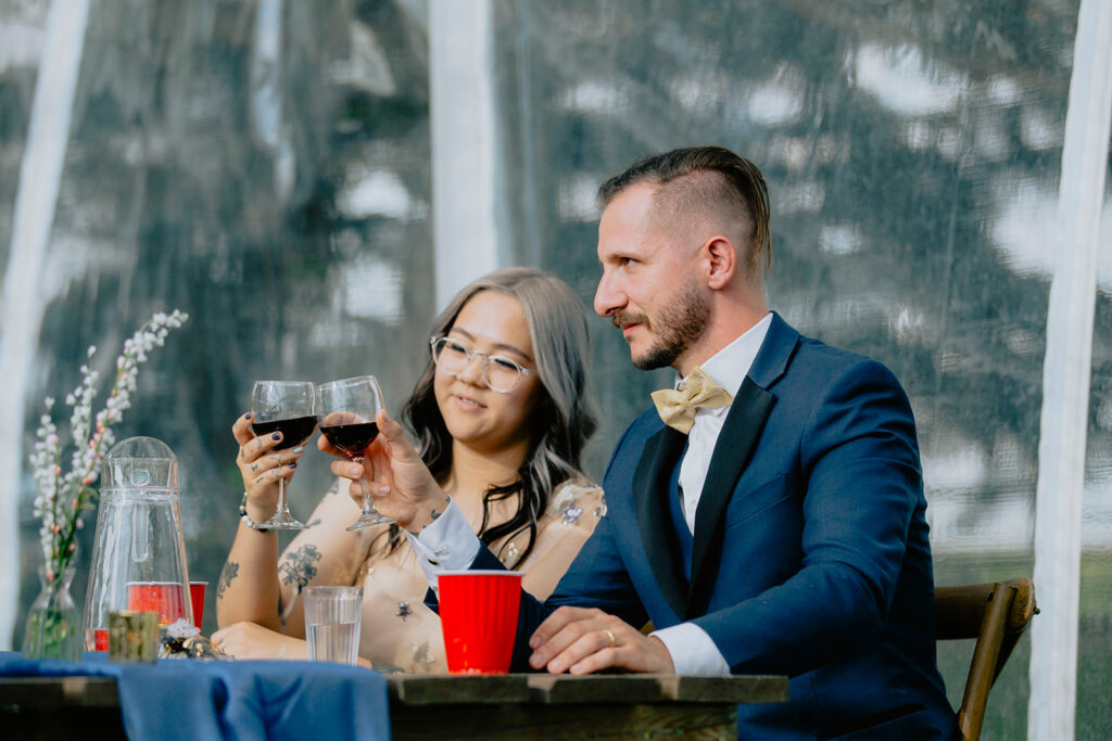 A bride and groom toasting wine at a table in a tent.
